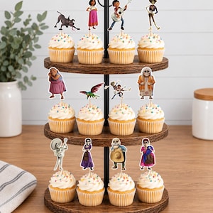 May include: A three-tiered wooden cupcake stand holding twelve cupcakes topped with white frosting and colourful sprinkles. Each cupcake features a paper cutout topper depicting various characters and creatures from the movie Coco.