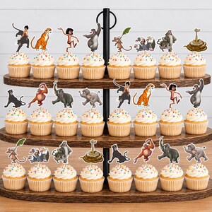 May include: A three-tiered wooden stand holding twenty-four cupcakes, each topped with a paper cutout of a character from The Jungle Book. The cupcakes feature white frosting with colorful sprinkles, arranged on dark brown oval wooden shelves.
