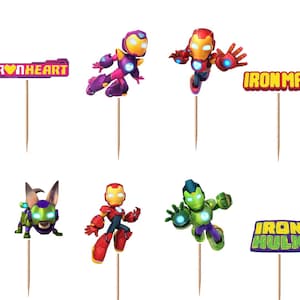May include: A set of decorative cupcake toppers featuring various superhero characters in red, gold, purple, and green armor, along with rectangular signs displaying the text IRONHEART, IRONMAN, and IRON HULK, all attached to thin wooden sticks.