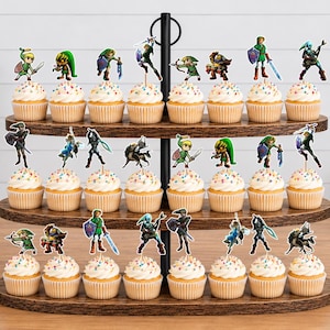 Op de afbeelding: Een houten standaard met drie niveaus en vierentwintig cupcakes, elk voorzien van een kleine papieren uitsparing van een videogamepersonage. De cupcakes hebben witte glazuur met kleurrijke hagelslag en staan op de donkerbruine houten planken.