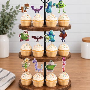 May include: A three-tiered wooden cupcake stand holding twelve cupcakes, each topped with a paper cutout of a character from the Monsters University film. The cupcakes feature white frosting with colorful sprinkles and are arranged on circular trays.