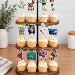 May include: A three-tiered wooden cupcake stand holding twelve cupcakes topped with colorful sprinkles and various character-themed paper toppers, including figures like a space ranger, a cowgirl, a spork, a horse, and a purple camera.