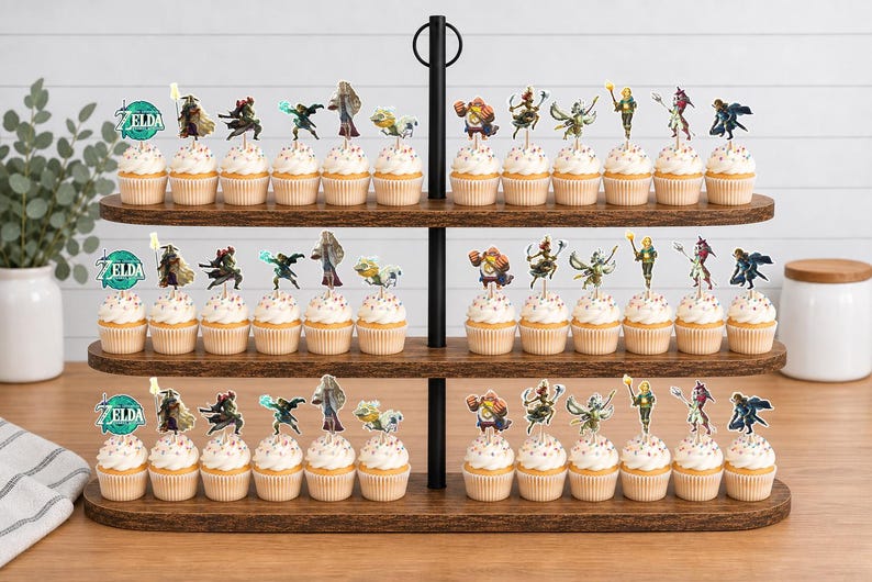 May include: A three-tiered wooden cupcake stand holding numerous cupcakes topped with various Legend of Zelda character paper toppers. Each topper features a unique character illustration or the circular teal Zelda logo with white text.