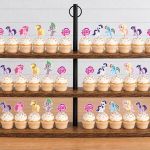 Op de afbeelding: Een houten cupcake-standaard met drie niveaus met talloze cupcakes, bekroond met My Little Pony-papieren toppers. Elke topper bevat een kleurrijke pony- of drakenillustratie en het My Little Pony-logo, gerangschikt in rijen op de donkere houten planken.