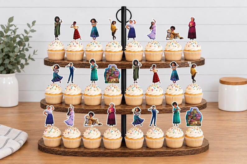 Pode incluir: Um suporte de madeira para cupcakes de tr&ecirc;s n&iacute;veis com vinte e quatro cupcakes, cada um decorado com um recorte de papel apresentando personagens e uma casa do filme Encanto. O suporte possui uma al&ccedil;a central de metal preto.