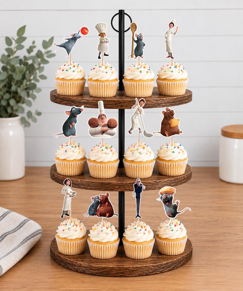 May include: A three-tiered wooden cupcake stand holding twelve cupcakes topped with white frosting and colorful sprinkles. Each cupcake features a decorative paper topper depicting various characters and culinary items from the movie Ratatouille.