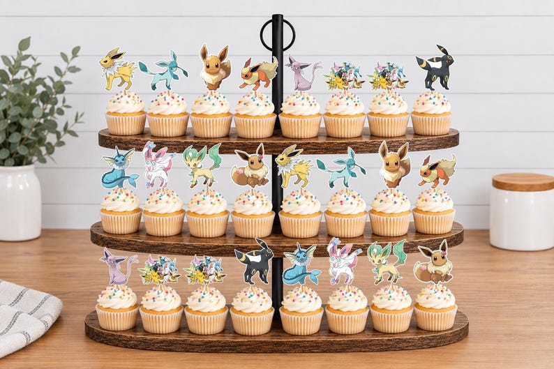 May include: A three-tiered wooden stand holding twenty-four cupcakes, each topped with a colorful paper cutout of various Eevee evolution characters. The cupcakes feature white frosting with multi-colored sprinkles, arranged in rows on the dark wood.