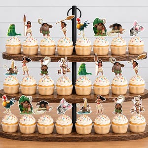 Op de afbeelding: Een houten cupcake-standaard met drie niveaus en vierentwintig cupcakes, elk voorzien van een decoratieve papieren uitsparing met personages en iconen uit de film Moana, waaronder Moana, Maui, Heihei, Pua en diverse tribale symbolen.