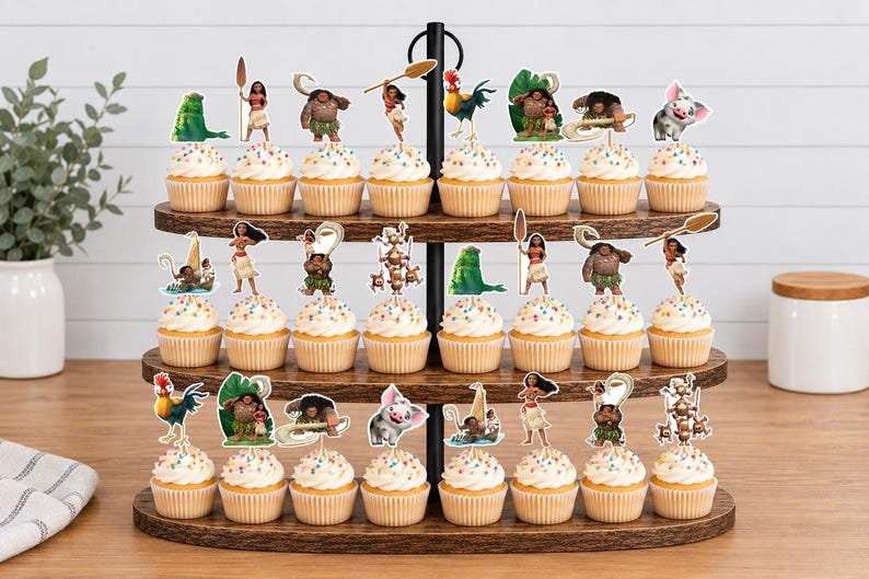 Op de afbeelding: Een houten cupcake-standaard met drie niveaus en vierentwintig cupcakes, elk voorzien van een decoratieve papieren uitsparing met personages en iconen uit de film Moana, waaronder Moana, Maui, Heihei, Pua en diverse tribale symbolen.