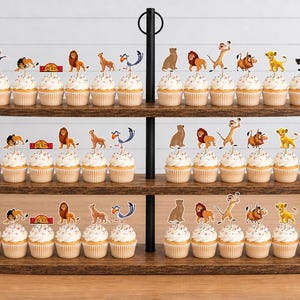 K&ouml;nnte beinhalten: Ein dreist&ouml;ckiger Cupcake-St&auml;nder aus Holz mit zahlreichen Cupcakes, die mit Papieraufstellern von Figuren aus Der K&ouml;nig der L&ouml;wen verziert sind, darunter Simba, Nala, Timon, Pumbaa, Zazu, Rafiki und Mufasa sowie ein rotes Schild mit The Lion King.