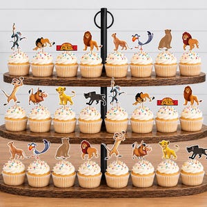 K&ouml;nnte beinhalten: Ein dreist&ouml;ckiger Cupcake-St&auml;nder aus Holz mit dreiundzwanzig Cupcakes, die mit Papieraufstellern von Charakteren aus Der K&ouml;nig der L&ouml;wen verziert sind, darunter Simba, Nala, Timon, Pumbaa, Zazu, Rafiki und Mufasa sowie rot-gelbe Logos.