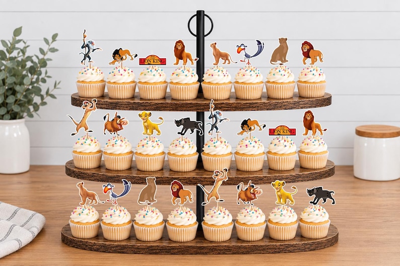 K&ouml;nnte beinhalten: Ein dreist&ouml;ckiger Cupcake-St&auml;nder aus Holz mit dreiundzwanzig Cupcakes, die mit Papieraufstellern von Charakteren aus Der K&ouml;nig der L&ouml;wen verziert sind, darunter Simba, Nala, Timon, Pumbaa, Zazu, Rafiki und Mufasa sowie rot-gelbe Logos.