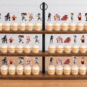 May include: A three-tiered wooden cupcake stand holding numerous cupcakes topped with Wreck-It Ralph character paper toppers. The toppers feature various figures including Vanellope, Ralph, Felix, and racing cars, all arranged on white frosting.