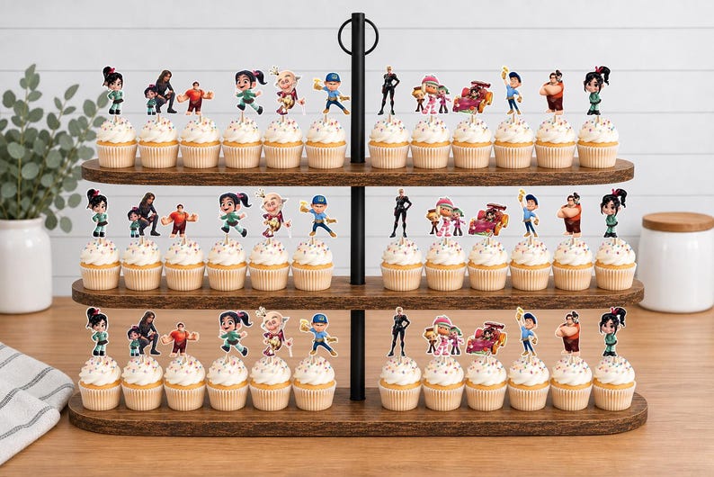 May include: A three-tiered wooden cupcake stand holding numerous cupcakes topped with Wreck-It Ralph character paper toppers. The toppers feature various figures including Vanellope, Ralph, Felix, and racing cars, all arranged on white frosting.