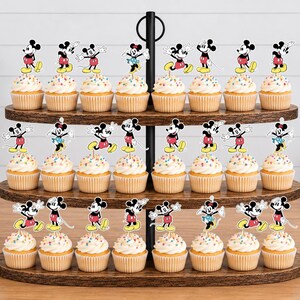 K&ouml;nnte beinhalten: Ein dreist&ouml;ckiger Cupcake-St&auml;nder aus Holz mit vierundzwanzig Cupcakes, die jeweils mit einem bunten Papieraufsteller von Mickey oder Minnie Mouse in verschiedenen Posen verziert sind. Die Cupcakes haben wei&szlig;e Glasur mit bunten Streuseln.