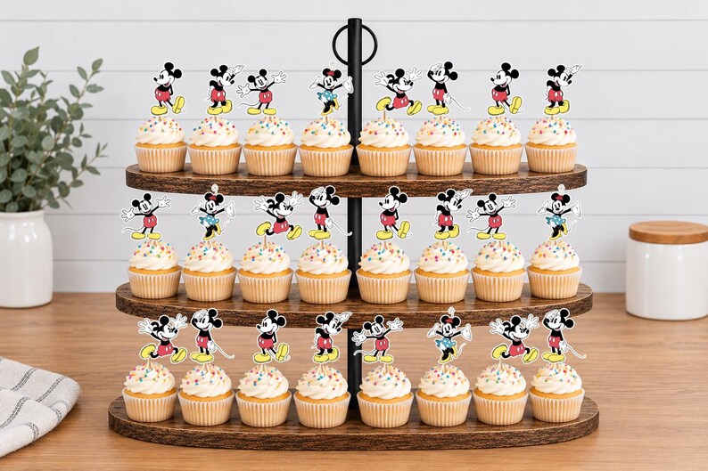 K&ouml;nnte beinhalten: Ein dreist&ouml;ckiger Cupcake-St&auml;nder aus Holz mit vierundzwanzig Cupcakes, die jeweils mit einem bunten Papieraufsteller von Mickey oder Minnie Mouse in verschiedenen Posen verziert sind. Die Cupcakes haben wei&szlig;e Glasur mit bunten Streuseln.
