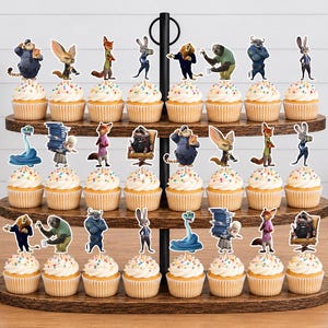 Pu&ograve; includere: Un'alzata per cupcake in legno a tre livelli contenente ventiquattro cupcake, ognuno sormontato da una sagoma di carta colorata di un personaggio di Zootopia. I cupcake hanno una glassa bianca con zuccherini multicolori sui ripiani in legno.