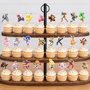 May include: A three-tiered wooden cupcake stand holding twenty-four cupcakes, each topped with a colorful paper cutout of a video game character. The stand features a central black metal rod and oval-shaped shelves with a dark brown wood grain finish.