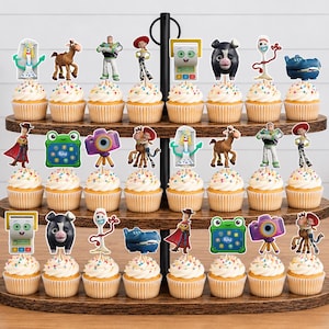 May include: A three-tiered wooden cupcake stand holding twenty-two cupcakes, each topped with a decorative paper cutout featuring various animated characters including a white spork, a brown horse, a green frog, and a purple camera on a tripod.