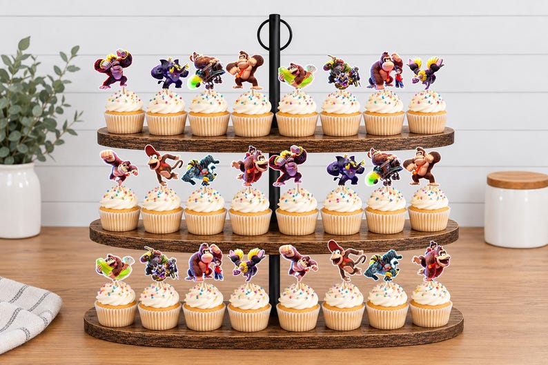 May include: A three-tiered wooden cupcake stand holding twenty-two cupcakes, each topped with a colorful paper cutout of Donkey Kong characters. The stand features a central black metal rod with a ring handle at the top, displaying various poses.