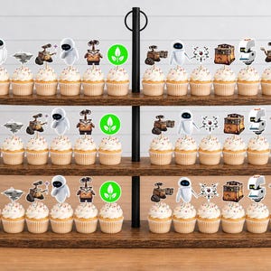 May include: A three-tiered wooden stand holding rows of cupcakes topped with paper cutouts featuring characters and icons from the movie WALL-E, including the robots WALL-E and EVE, a green plant symbol, and various mechanical components on white sticks.