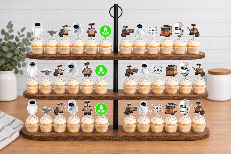 May include: A three-tiered wooden stand holding rows of cupcakes topped with paper cutouts featuring characters and icons from the movie WALL-E, including the robots WALL-E and EVE, a green plant symbol, and various mechanical components on white sticks.