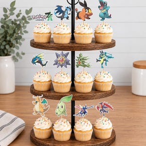 K&ouml;nnte beinhalten: Ein dreist&ouml;ckiger Cupcake-St&auml;nder aus Holz mit zw&ouml;lf Cupcakes, die mit wei&szlig;em Zuckerguss, bunten Streuseln und verschiedenen Pok&eacute;mon-Figuren aus Papier verziert sind, darunter ein Pok&eacute;mon Legends Z-A Logo-Topper.