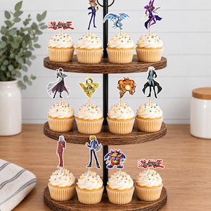 K&ouml;nnte beinhalten: Ein dreist&ouml;ckiger Cupcake-St&auml;nder aus Holz mit zw&ouml;lf Cupcakes, die mit bunten Streuseln und Yu-Gi-Oh!-Papieraufsteckern verziert sind. Die Aufstecker zeigen verschiedene Charaktere, Monster, das Millennium-Puzzle und das rote Logo.