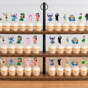 May include: A three-tiered wooden cupcake stand holding rows of cupcakes topped with colorful paper character cutouts. The decorations feature various animated figures including blue and pink creatures, a surfer, and a person in a red dress.