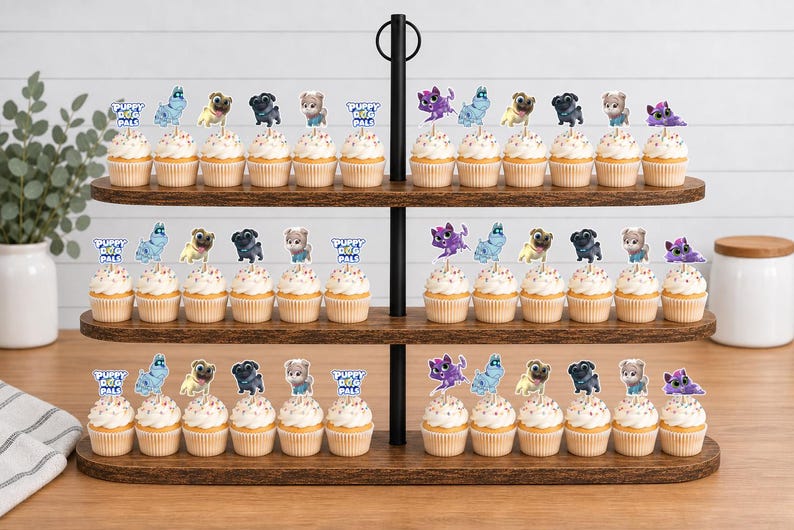 Puede incluir: Un soporte de madera de tres niveles con numerosos cupcakes cubiertos con recortes de papel decorativos. Los adornos presentan personajes de dibujos animados y el texto Puppy Dog Pals. Cada cupcake tiene glaseado blanco y est&aacute; en filas.
