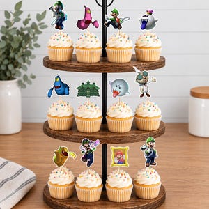May include: A three-tiered wooden cupcake stand holding twelve cupcakes topped with white frosting and colorful sprinkles. Each cupcake features a decorative paper topper depicting various characters and elements from the Luigi's Mansion video game series.