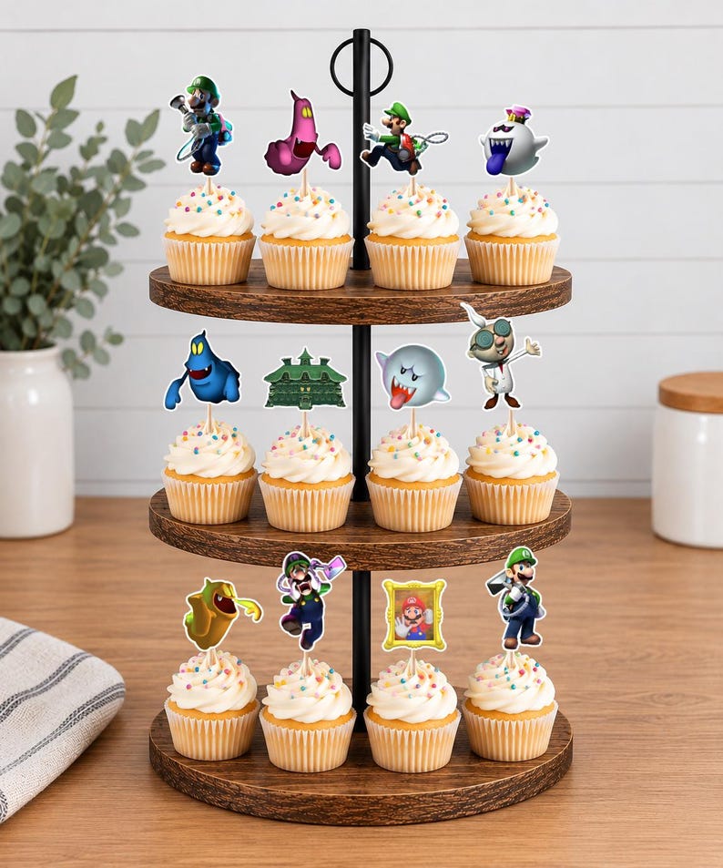 May include: A three-tiered wooden cupcake stand holding twelve cupcakes topped with white frosting and colorful sprinkles. Each cupcake features a decorative paper topper depicting various characters and elements from the Luigi's Mansion video game series.