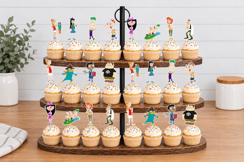 May include: A three-tiered wooden cupcake stand holding twenty-four cupcakes, each topped with a colorful paper cutout of characters from Phineas and Ferb, including Phineas, Ferb, Isabella, Candace, Perry the Platypus, and Dr. Doofenshmirtz.