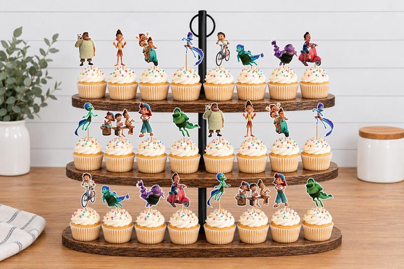 Puede incluir: Un soporte de madera para cupcakes de tres niveles con veinticuatro cupcakes, cada uno decorado con un peque&ntilde;o recorte de papel de personajes de la pel&iacute;cula Luca. Los cupcakes muestran varias escenas con los personajes en acci&oacute;n.