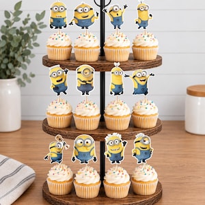 May include: A three-tiered wooden cupcake stand holding twelve cupcakes, each topped with a white frosting swirl, colorful sprinkles, and a decorative paper cutout of a yellow Minion character wearing blue overalls in various poses.