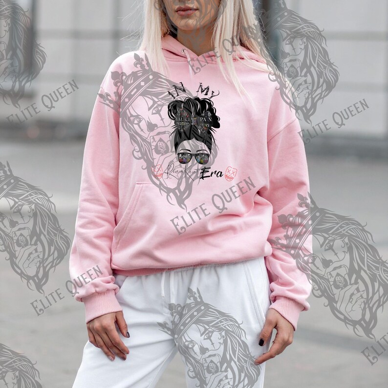 May include: A light pink hoodie with a front graphic of a woman with sunglasses and a messy bun. The text "In My Always Era" is printed on the front. The hoodie has a kangaroo pocket and a drawstring hood.