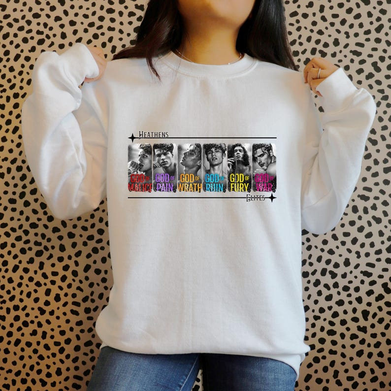K&ouml;nnte beinhalten: Wei&szlig;er Pullover mit einem Grafikdruck von f&uuml;nf M&auml;nnergesichtern mit dem Text "GOD OF" und einem Wort in einer anderen Farbe unter jedem Gesicht. Die W&ouml;rter sind "GOD OF CHAOS", "GOD OF PAIN", "GOD OF WRATH", "GOD OF RUIN", "GOD OF FURY" und "GOD OF WAR". Der Text "HEATHENS" befindet sich &uuml;ber der Grafik und der Text "BURNS" unter der Grafik.