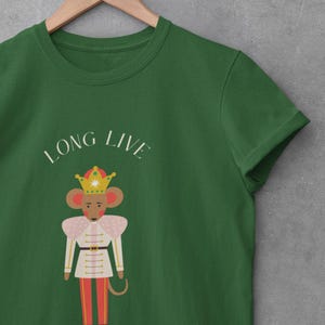 May include: Green t-shirt with the text "LONG LIVE THE QUEEN". The shirt features a cartoon mouse wearing a crown and a military-style uniform in white, pink, and red. The design is centered on the shirt.
