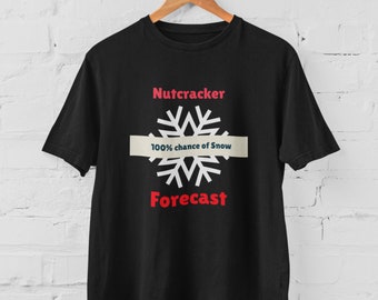Può includere: T-shirt nera con le parole "Nutcracker Forecast" in rosso e un fiocco di neve bianco. Il testo "100% chance of Snow" è centrato su un rettangolo orizzontale beige chiaro.