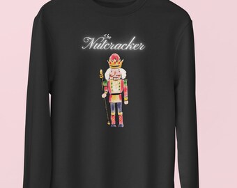 May include: Black sweatshirt with a watercolor illustration of a Nutcracker soldier. The Nutcracker is wearing a red and gold uniform, a crown, and holding a staff. The text "The Nutcracker" is written above the illustration in a cursive font.