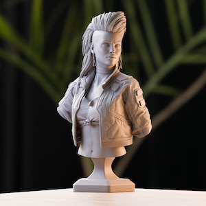 Può includere: Un busto in scultura grigia di una donna con un taglio di capelli mohawk che indossa una giacca e una maglietta. Il busto è su un piedistallo.