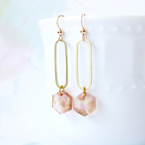 May include: Gold dangle earrings with a pink and white hexagonal shaped pendant.