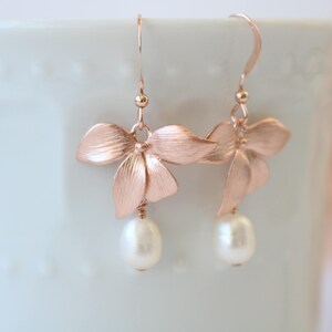 May include: Rose gold earrings with a delicate flower design and a pearl drop.