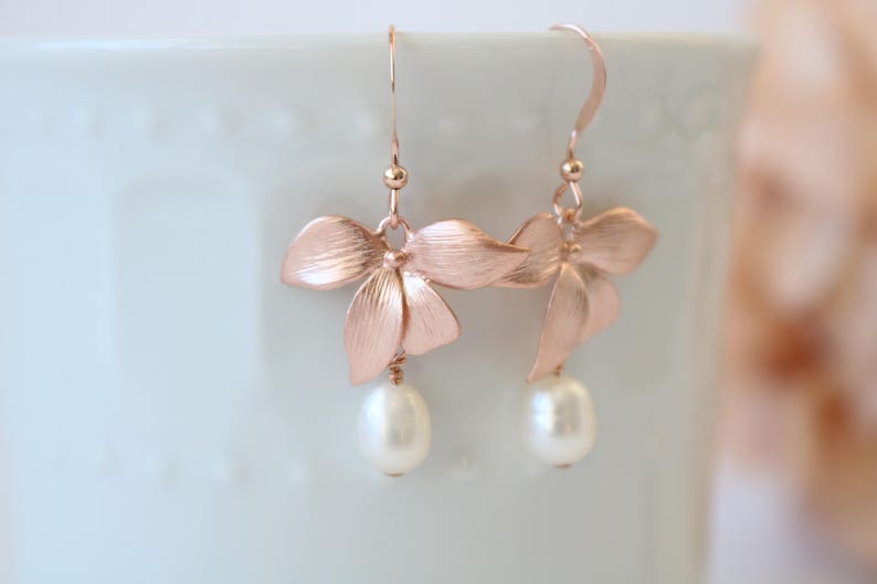 May include: Rose gold earrings with a delicate flower design and a pearl drop.