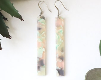 May include: A pair of long, rectangular earrings with a marbled, multi-coloured design in shades of pink, green, and grey. The earrings have silver hooks.