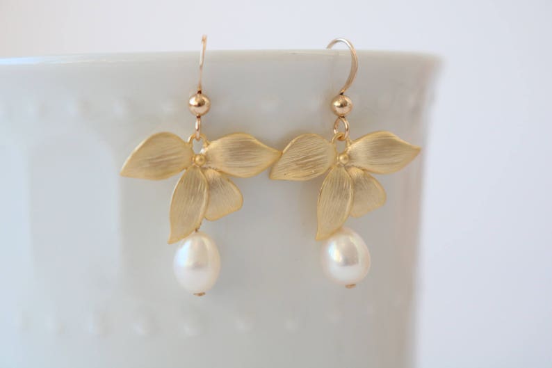 May include: Gold flower earrings with a single pearl dangling from each earring.