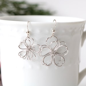 May include: Silver flower-shaped dangle earrings with a delicate wire design.