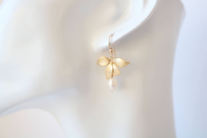 May include: Gold flower earrings with a single pearl dangling from the bottom.
