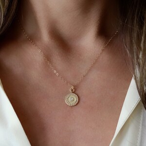 May include: A gold chain necklace with a round pendant featuring a white opal surrounded by small clear stones.