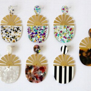 Pode incluir: Seis pares de brincos dourados com um design de sol. Cada brinco apresenta um padr&atilde;o diferente na metade inferior, incluindo listras pretas e brancas, tartaruga, branco marmorizado e glitter de v&aacute;rias cores.